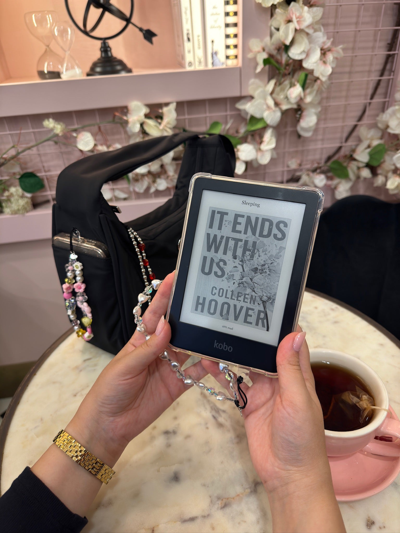 This image includes a lifestyle shot in a cafe with an e-book and a purse and a cup of tea in the background. The image features Hatossa phone charms.