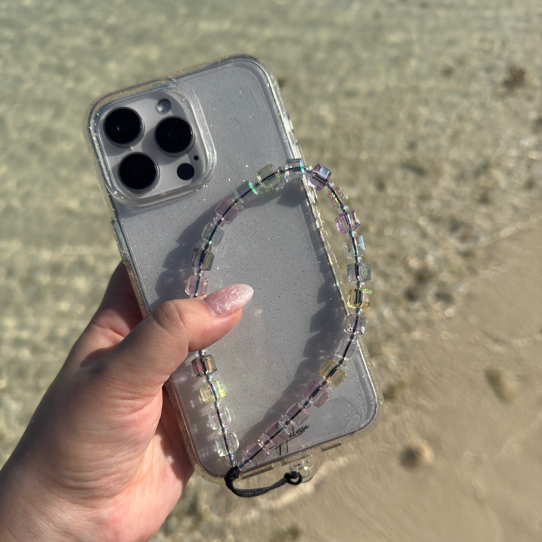 Aura Hatossa Phone Charm attached to a phone and held in a hand, the background is a beach.
