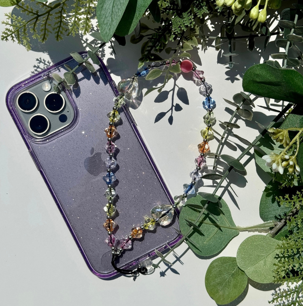 iPhone used as a prop to show Dream phone charm. The image also includes green leaves as a prop.