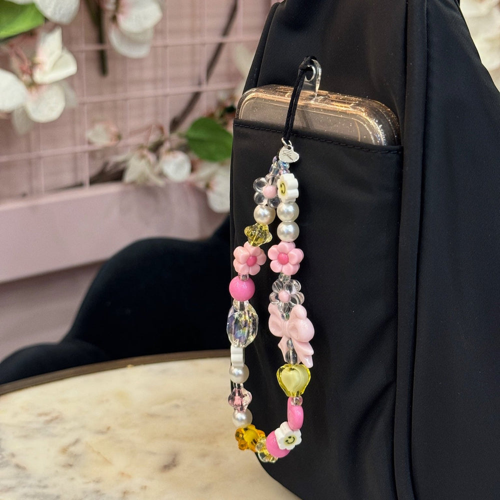 Image shows the Hatossa HONEY phone strap, phone charm, with the universal lanyard holder that is used on a phone. The phone is inside a bag.
