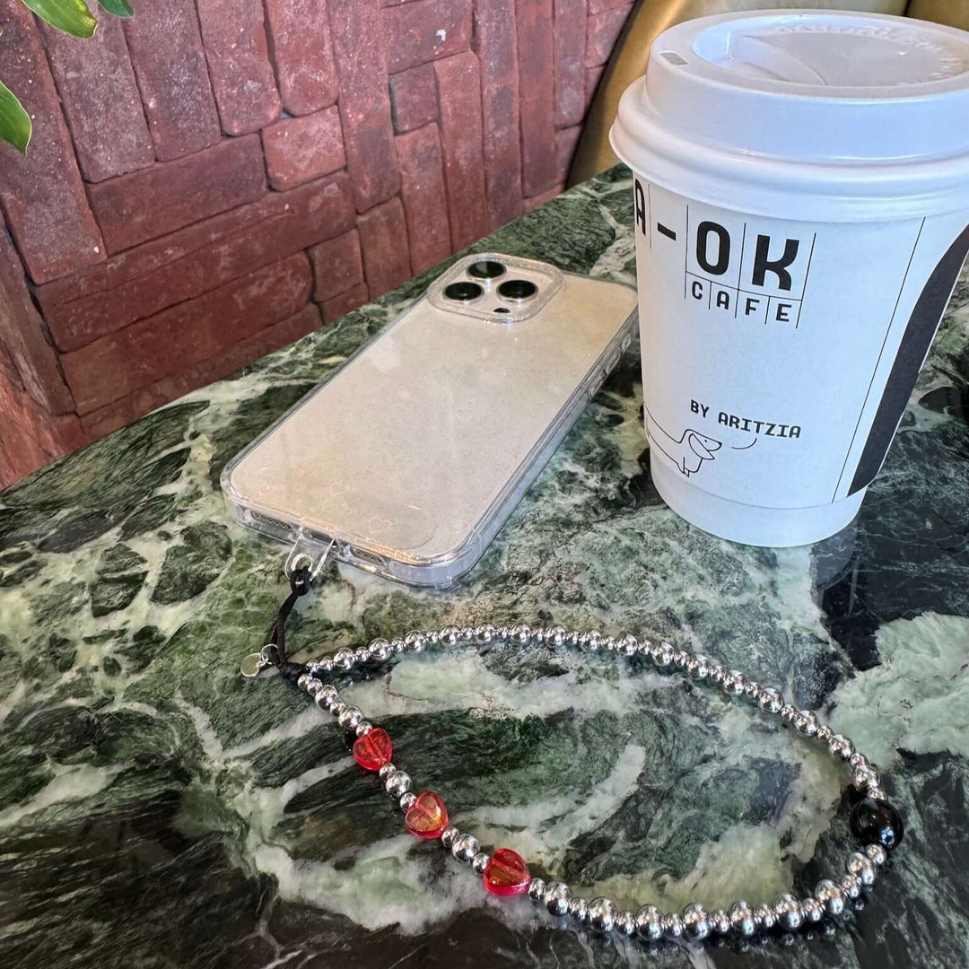 Image shows the Hatossa NOVA phone strap, phone charm, with the universal lanyard holder that can be used with any device, ebook, airpods. Image also shows a coffee cup