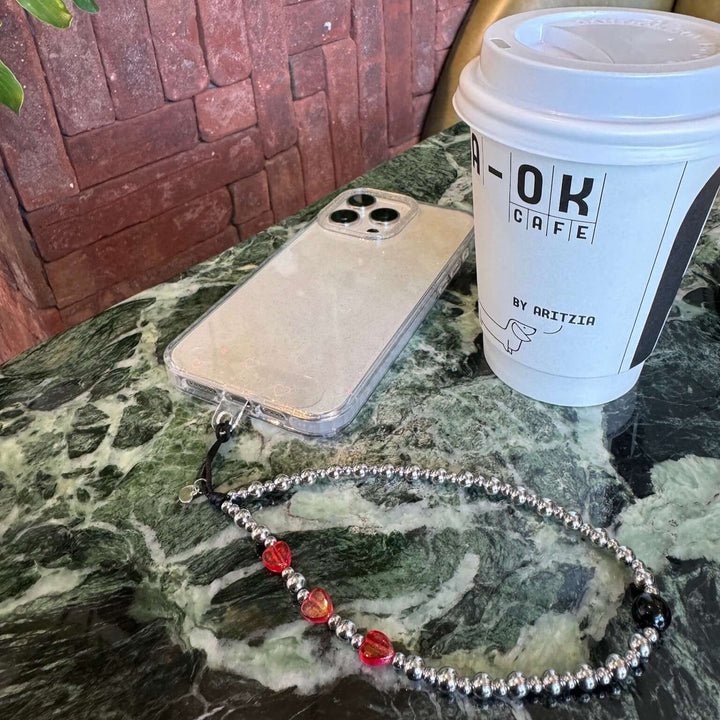 Image shows the Hatossa NOVA phone strap, phone charm, with the universal lanyard holder that can be used with any device, ebook, airpods. Image also shows a coffee cup
