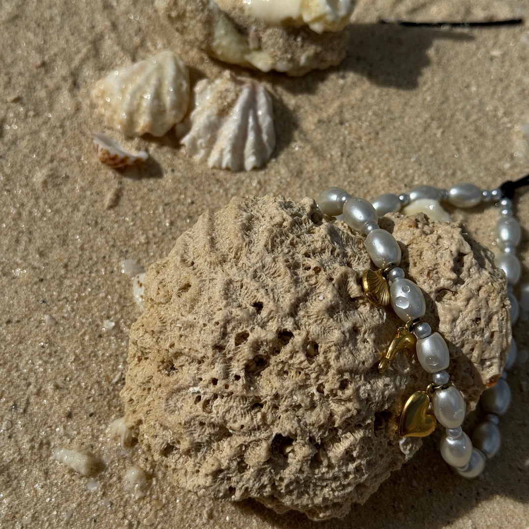 Ocean Hatossa Phone Charm leaning against a dried coral on the shore at the beach.