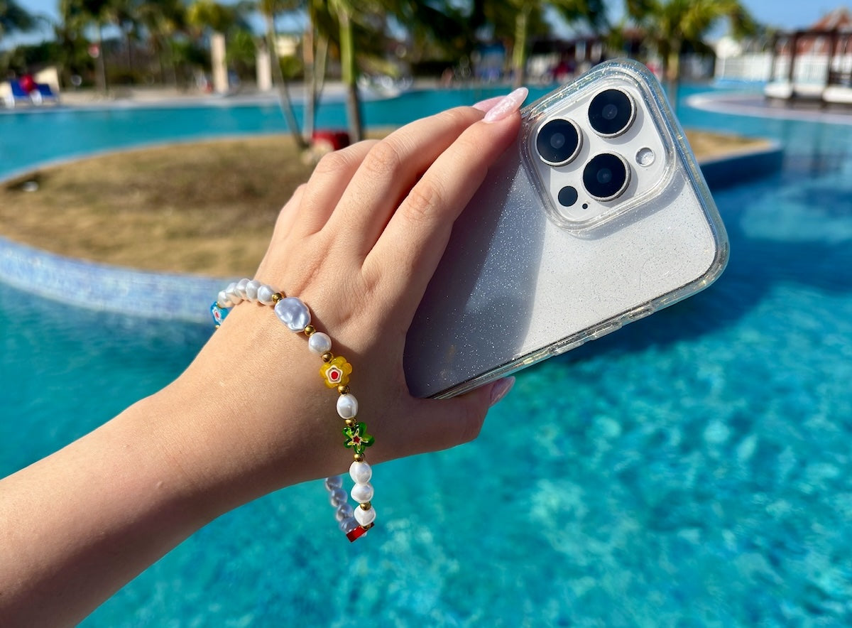 Summer Hatossa Phone charm attached to a phone held in a hand over a swimming pool  with palm trees in the background.