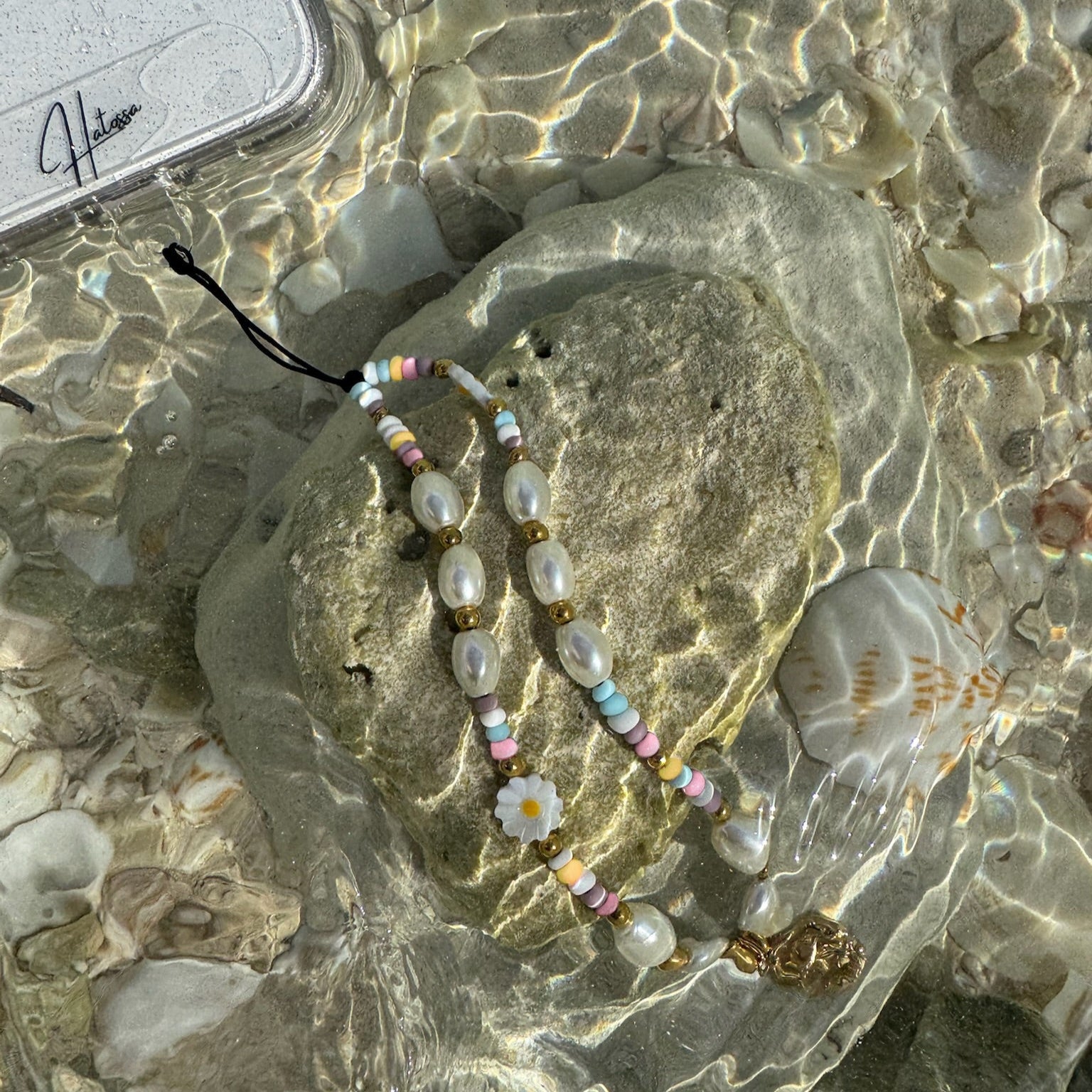 Treasure Hatossa phone charm attached to a phone. the charm is leaning against a rock under water in the ocean.